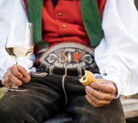 Un uomo che porta un costume tradizionale tiene in mano un calice di vino bianco e uno spuntino