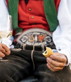 Un uomo che porta un costume tradizionale tiene in mano un calice di vino bianco e uno spuntino