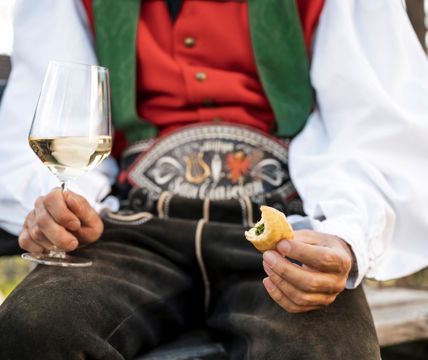 Un uomo che porta un costume tradizionale tiene in mano un calice di vino bianco e uno spuntino