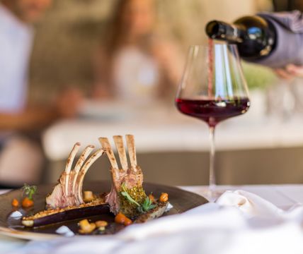 Carré d'agnello impiattato con verdure e vino rosso in un elegante ristorante