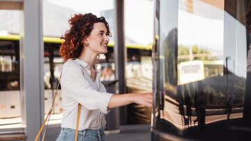Donna sale sorridendo su un autobus verde a una fermata moderna.