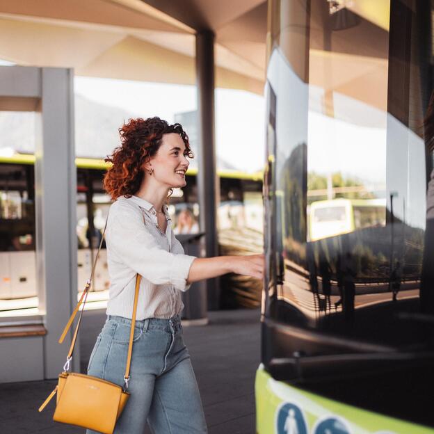 Donna sale sorridendo su un autobus verde a una fermata moderna.