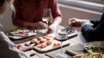 Tre persone gustano una merenda altoatesina con vino, formaggio, speck e affettati.