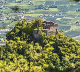Rovine su una collina boscosa, circondate da campi verdi e paesi nella valle.