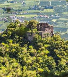 Rovine su una collina boscosa, circondate da campi verdi e paesi nella valle.