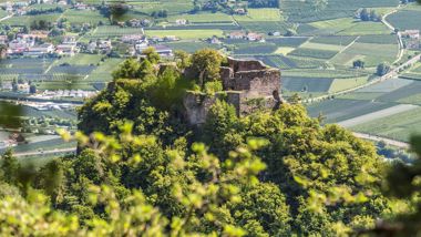 Rovine su una collina boscosa, circondate da campi verdi e paesi nella valle.