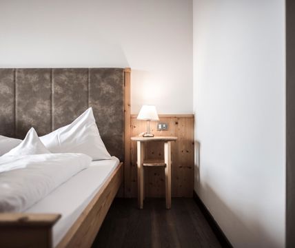 Camera da letto accogliente con letto in legno, testiera imbottita, biancheria bianca e comodino con lampada.
