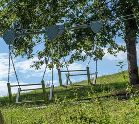 Due altalene in metallo sospese a un sistema di funi su un prato sotto gli alberi.